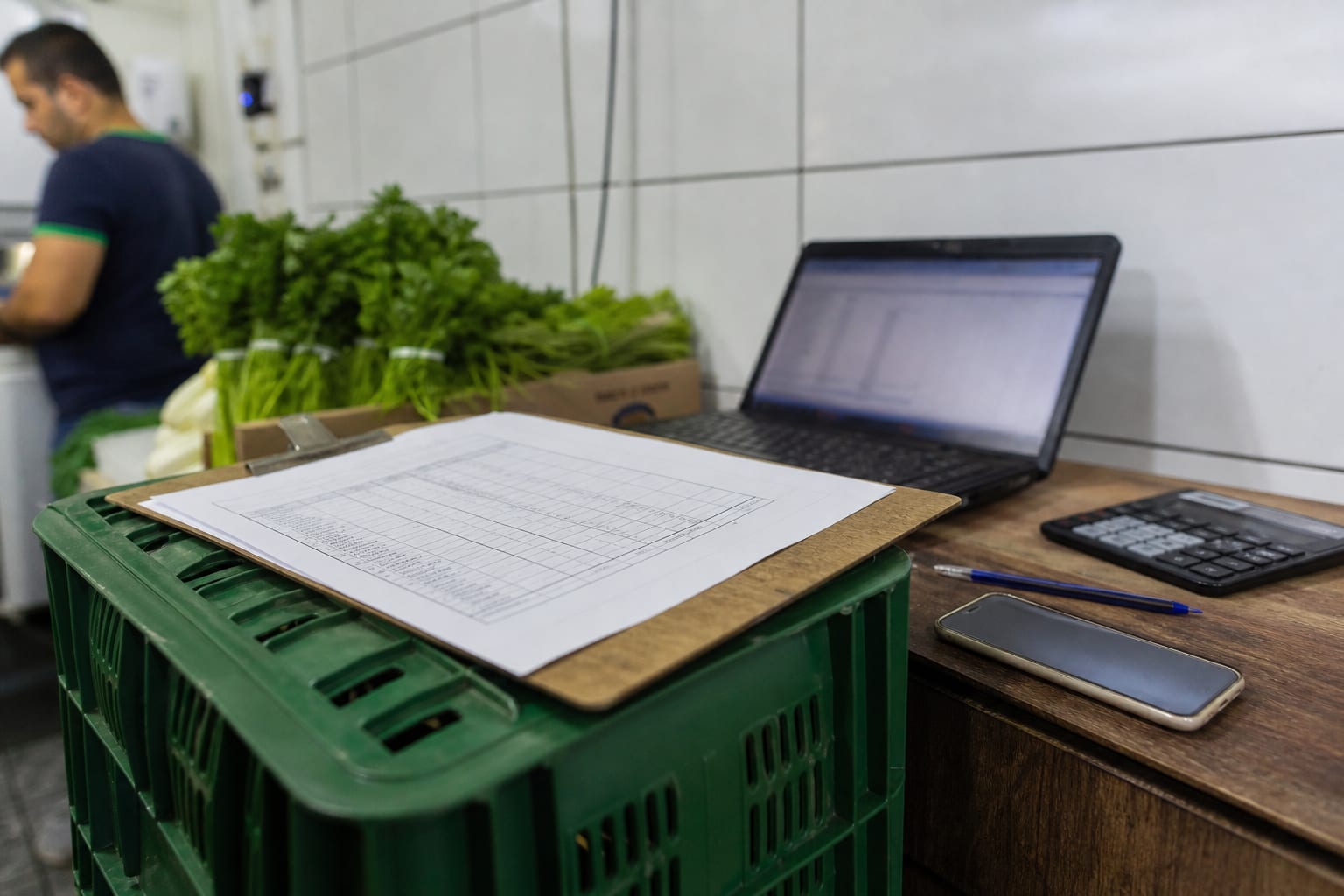 Prancheta, notebook com planilha e celular sobre bancada nos fundos de um mercadinho